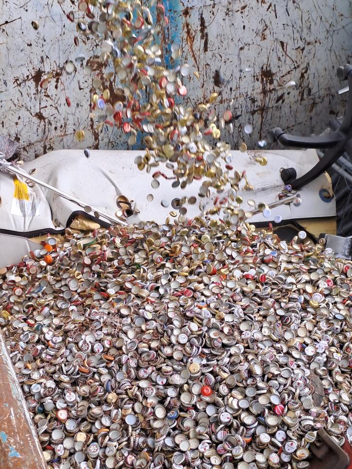 Countless collected crown caps fall into a collection container for scrap metal