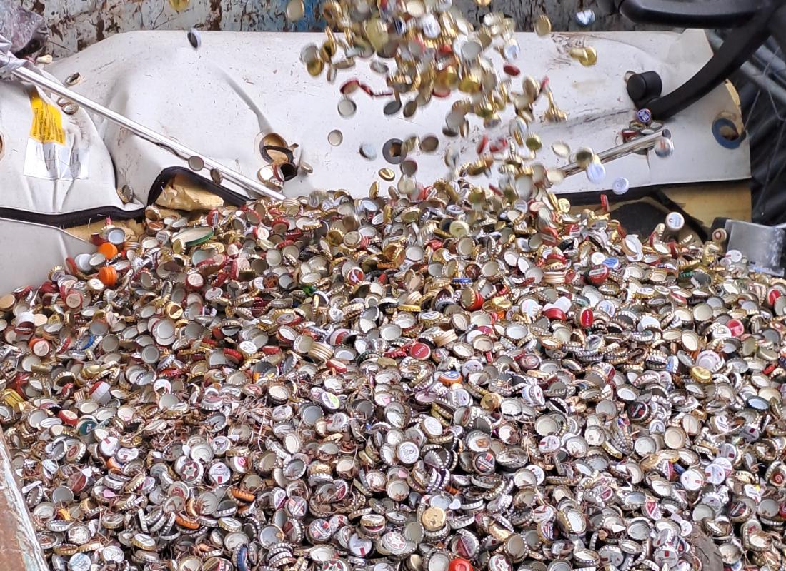 Unzählige gesammelte Kronkorken fallen in einen Sammelcontainer für Schrott