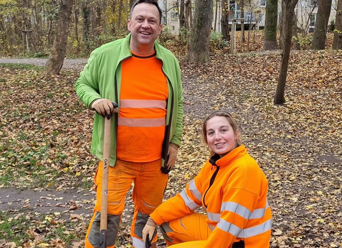 Zwei Gärtner in einer herbstlichen Grünanlage mit Blumenzwiebeln und Schaufel 